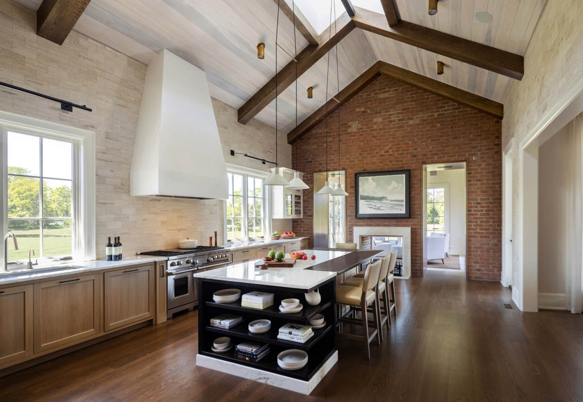 View of vaulted ceiling kitchen area with skylights, island with seating, stove and fireplace.